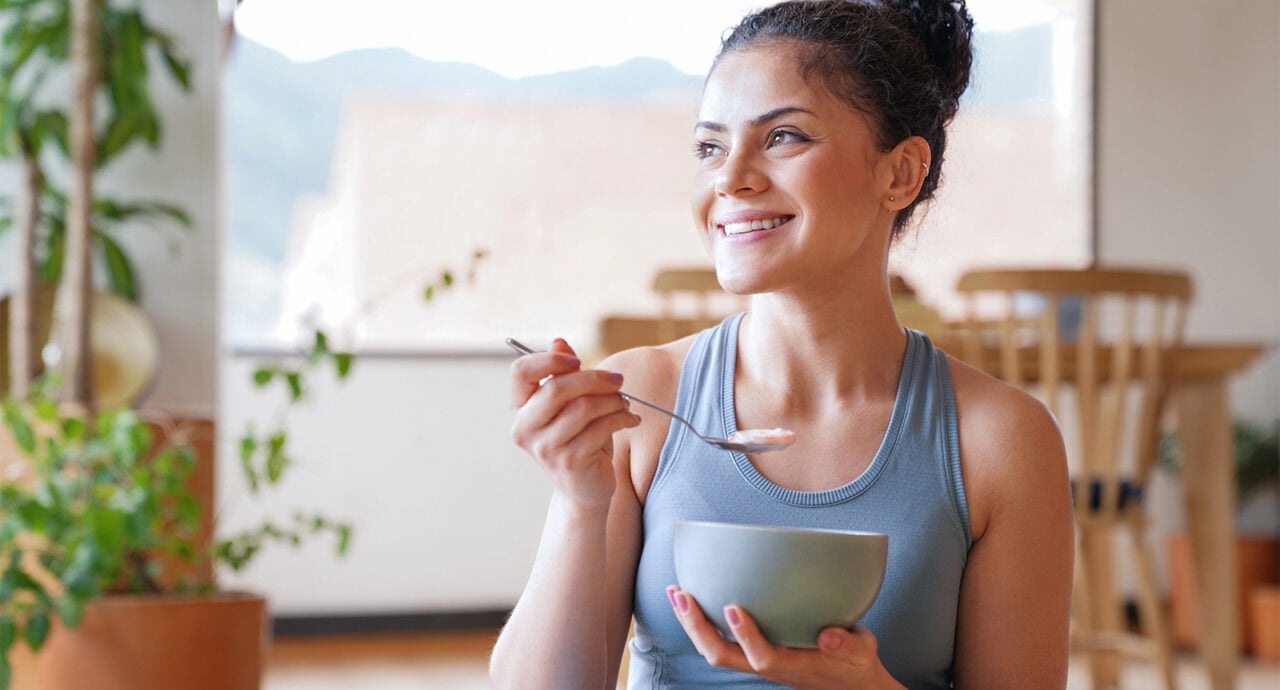 Glad kvinna i träningskläder äter yoghurt.