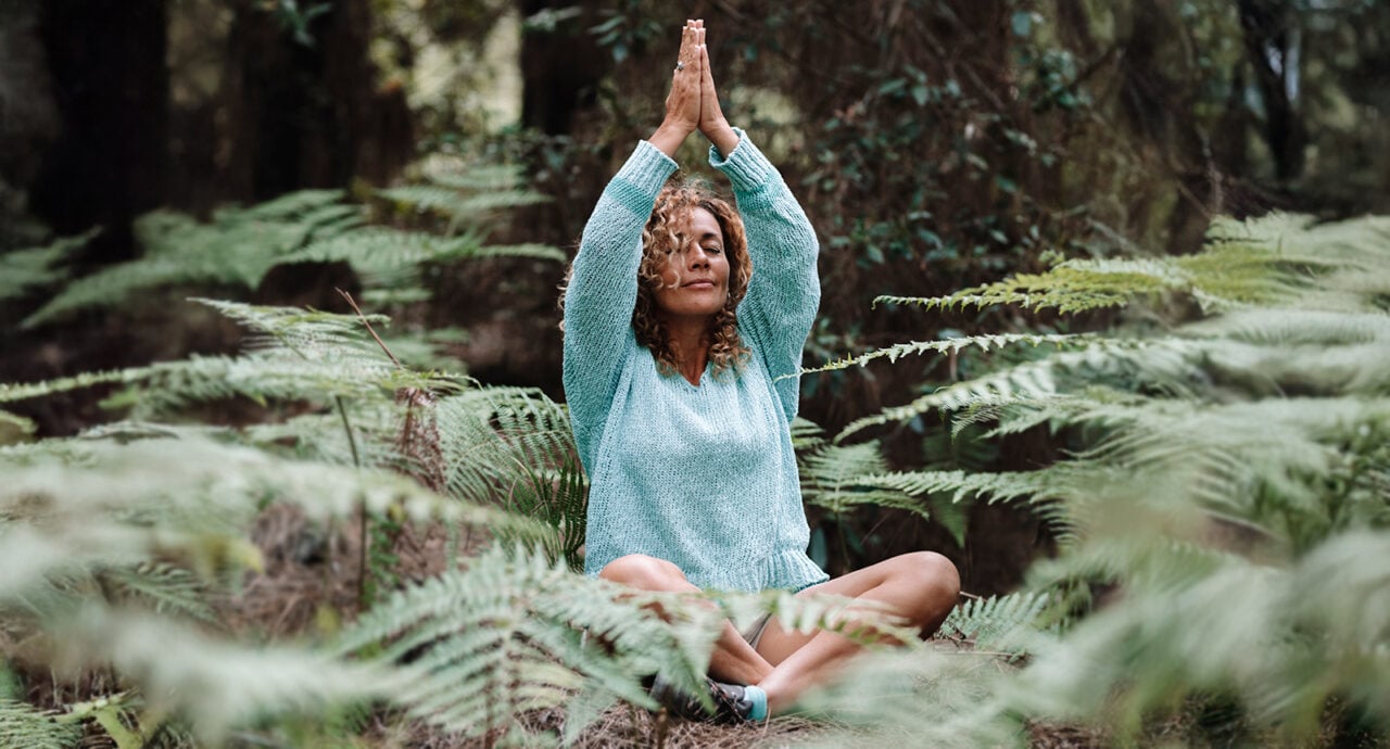 Medelålderskvinna mediterar i skogen.